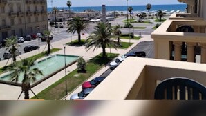 Un hotel con piscina, vistas al mar y una calle con coches y palmeras.