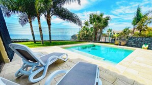 Un espace aménagé au bord de la piscine, avec deux chaises longues, une vue dégagée sur la piscine et un mur de pierre en arrière-plan.