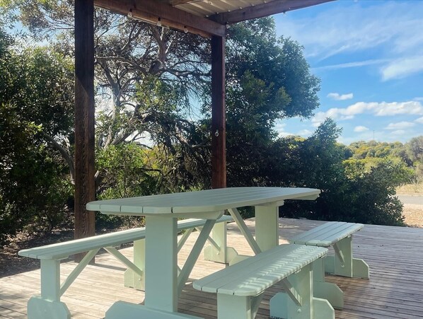 Una mesa de picnic sobre una terraza de madera con una pérgola encima.