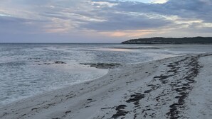 Une plage avec un rivage sablonneux et un promontoire rocheux à l’horizon.