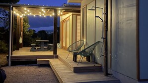 Un espace extérieur aménagé en terrasse, avec un sol en bois, deux chaises vertes, une table et des guirlandes lumineuses.