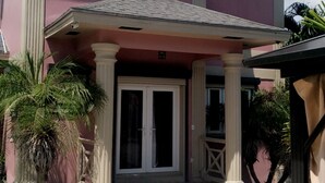 A two-story house with a pink facade, a front porch with columns, and a tiled roof. - A peice of paradise,large luxury condominium beautiful space cozy & homely!!!!!! (Nassau)