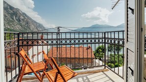 Ein Balkon mit zwei Holzstühlen, einem Metallgeländer und Blick auf einen Berg sowie ein Gewässer.