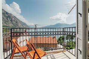 Uma varanda com duas cadeiras de madeira, guarda-corpo de metal e vista para uma montanha e um corpo de água.