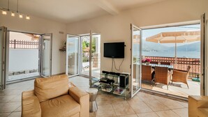 Ein Wohnzimmer mit einer Couch, einem Glastisch, einem Flachbildfernseher und einem Balkon mit Gartenmöbeln.