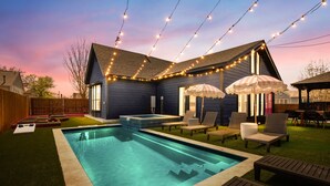 A backyard with a swimming pool, lounge chairs, and string lights.