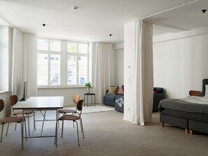 Een moderne, goed verlichte kamer met een eettafel, stoelen, een bank en een bed.