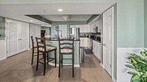 Una cocina compacta con una isla central, muebles blancos y una zona de comedor con dos sillas.
