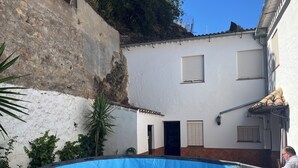 Ein Swimmingpool mit blauer Abdeckung, ein weißes Gebäude mit Fensterläden und eine Steinmauer.
