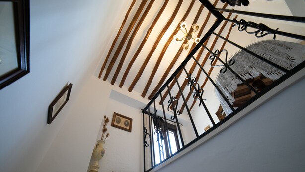 A staircase with a black metal railing, wooden beams, and a chandelier. - El Parador de Carmencita Casa Rural Capacidad 19 Personas (Almedinilla)