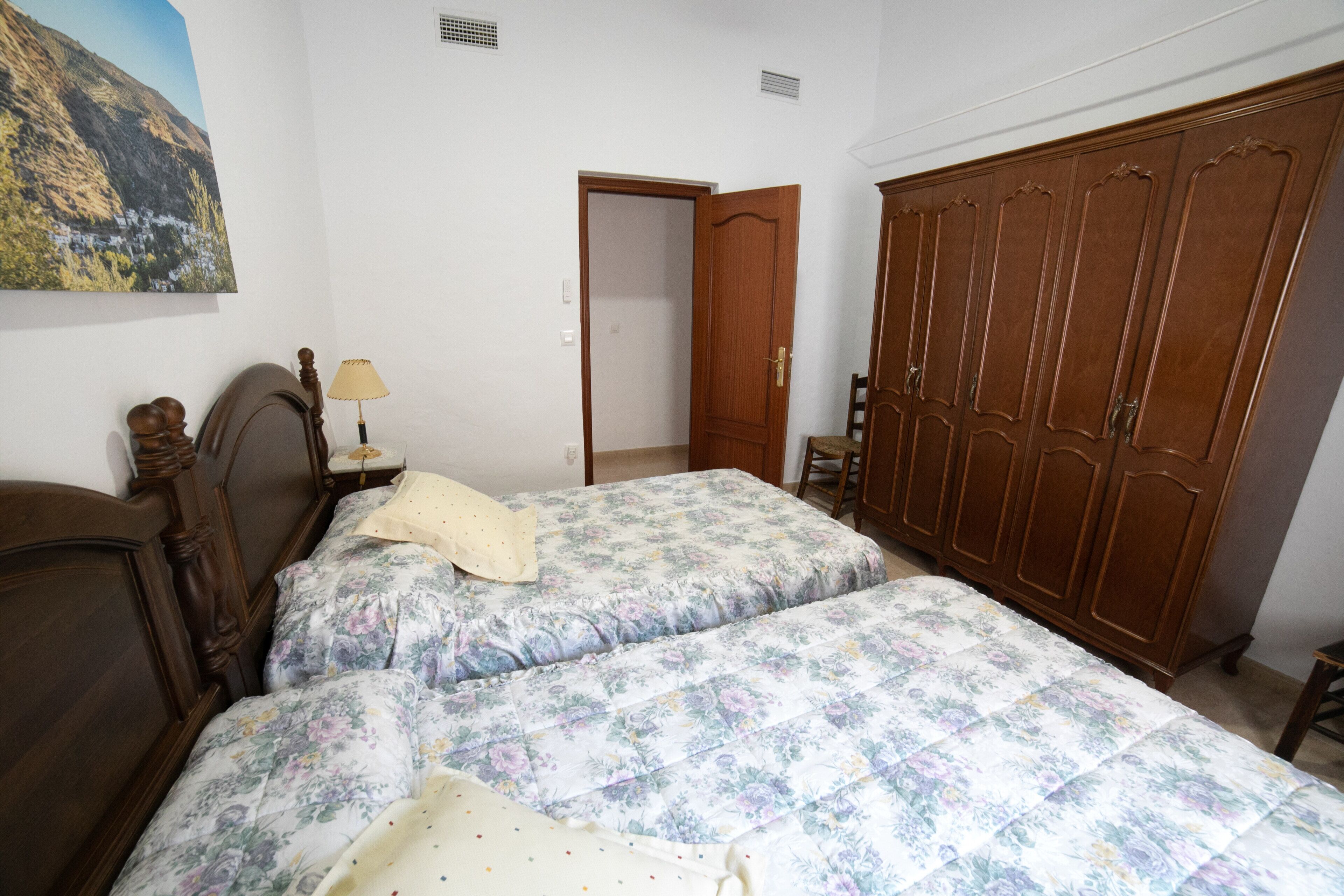 Een slaapkamer met twee bedden, een houten garderobe, een schilderij aan de muur en een deur naar een andere kamer.