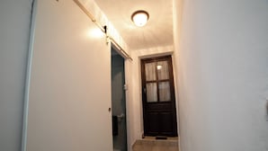 A narrow hallway with a door leading to a bathroom, a light fixture on the ceiling, and a small step at the door's entrance. - El Parador de Carmencita Casa Rural Capacidad 19 Personas (Almedinilla)