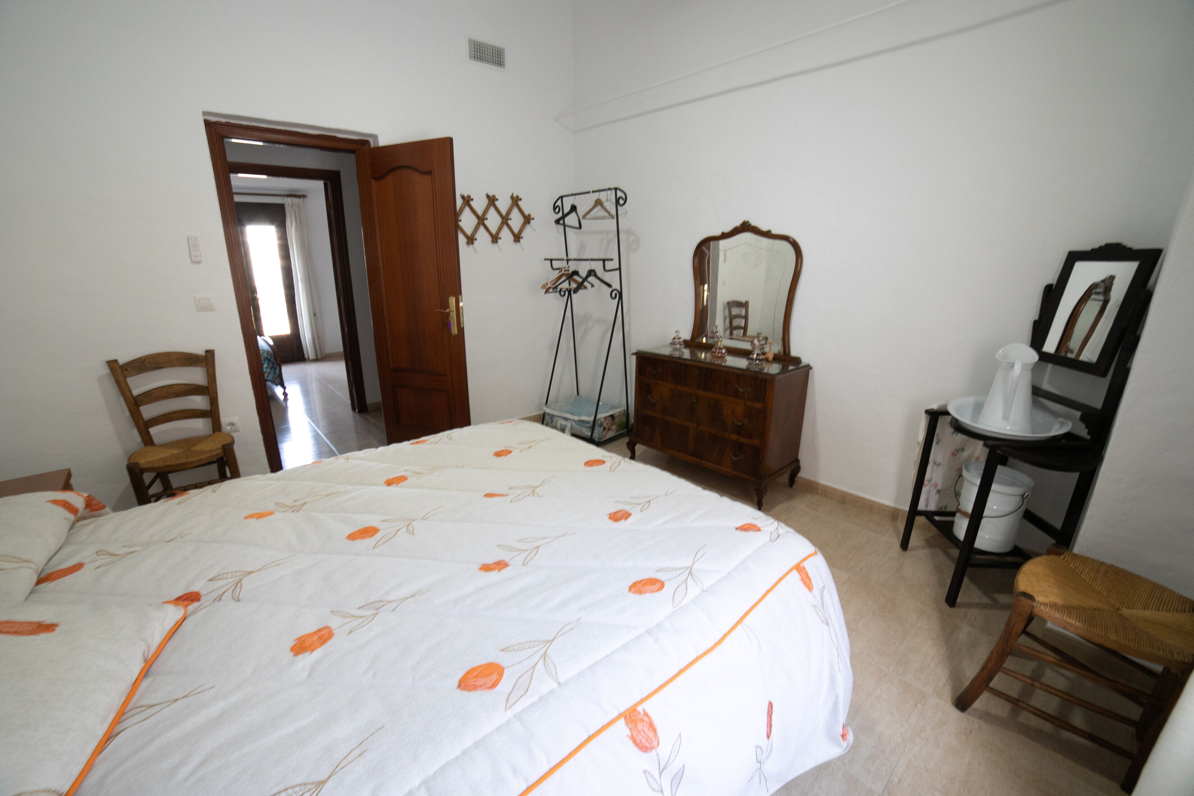 A bedroom with a bed, a wooden dresser, a mirror, a chair, and a small table.