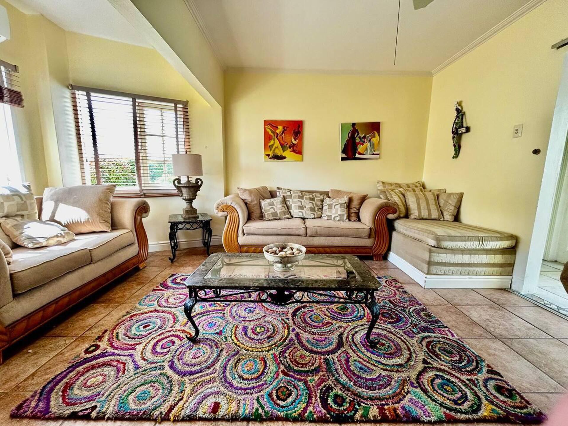 Ein Wohnzimmer mit einem beige farbenen Sofa, einem gemusterten Teppich und zwei Bildern an der Wand.