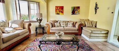 Ein Wohnzimmer mit einem beige farbenen Sofa, einem gemusterten Teppich und zwei Bildern an der Wand.