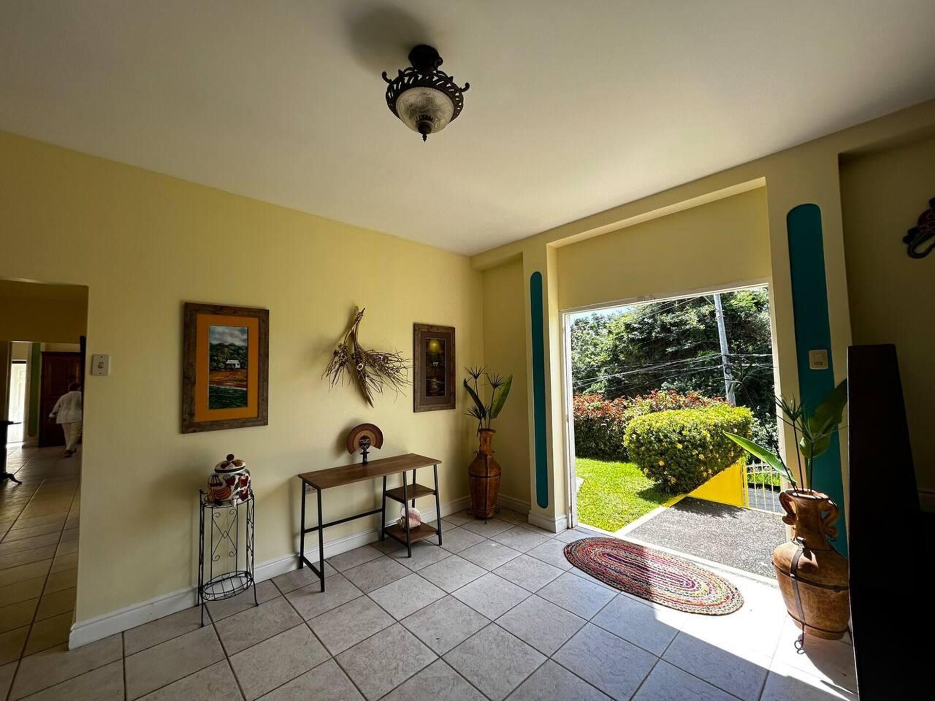 A spacious living room with a large window, a ceiling fan, and a door leading to a garden.