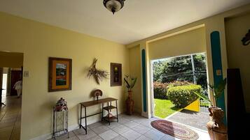 A spacious living room with a large window, a ceiling fan, and a door leading to a garden.