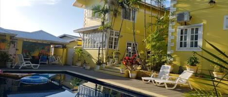 A yellow building with a swimming pool, white-framed windows, and potted plants.