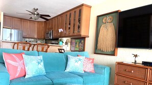 A living room with a teal sofa, wooden cabinets, a glass coffee table, and a flat-screen TV.