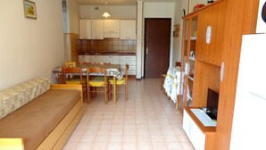 A compact kitchen with a dining area, a built-in bench, and a wooden cabinet. - Wonderful Apartment With Terrace and Pool (Caorle)