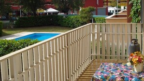 A balcony with a pool, white railing, and a table with a floral tablecloth. - Wonderful Apartment With Terrace and Pool (Caorle)