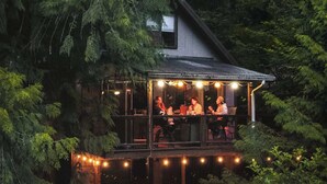 Una cabaña con terraza, rodeada de un bosque frondoso.