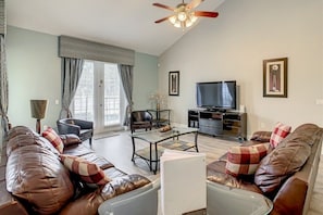 Una sala de estar con sofá, sillones, una mesa de centro, televisor y ventilador de techo.