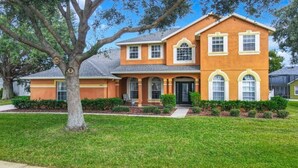 A two-story house with a front porch, a garage, and a well-maintained lawn. - Disney Dream! 10 Mins Away+Game Room, Pool & Hot Tub! - 101 Happy Memories Villa (Kissimmee)