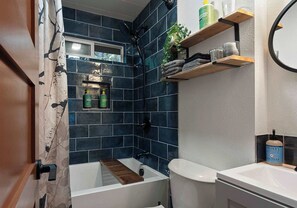 Une salle de bain avec une baignoire, des toilettes et un lavabo. On y trouve des étagères avec des articles de toilette et un miroir.