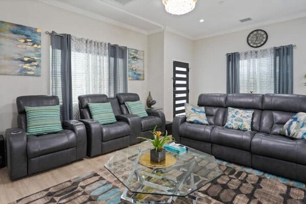 A living room with a dark leather sofa, two leather recliners, a glass coffee table, and a patterned rug.