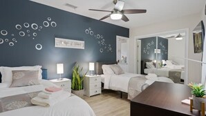 A modern hotel room with two beds, a ceiling fan, a large mirror, and a wooden desk.