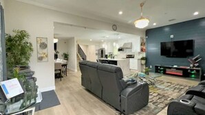 A modern living room with a sofa, a TV, and a dining area in the background.