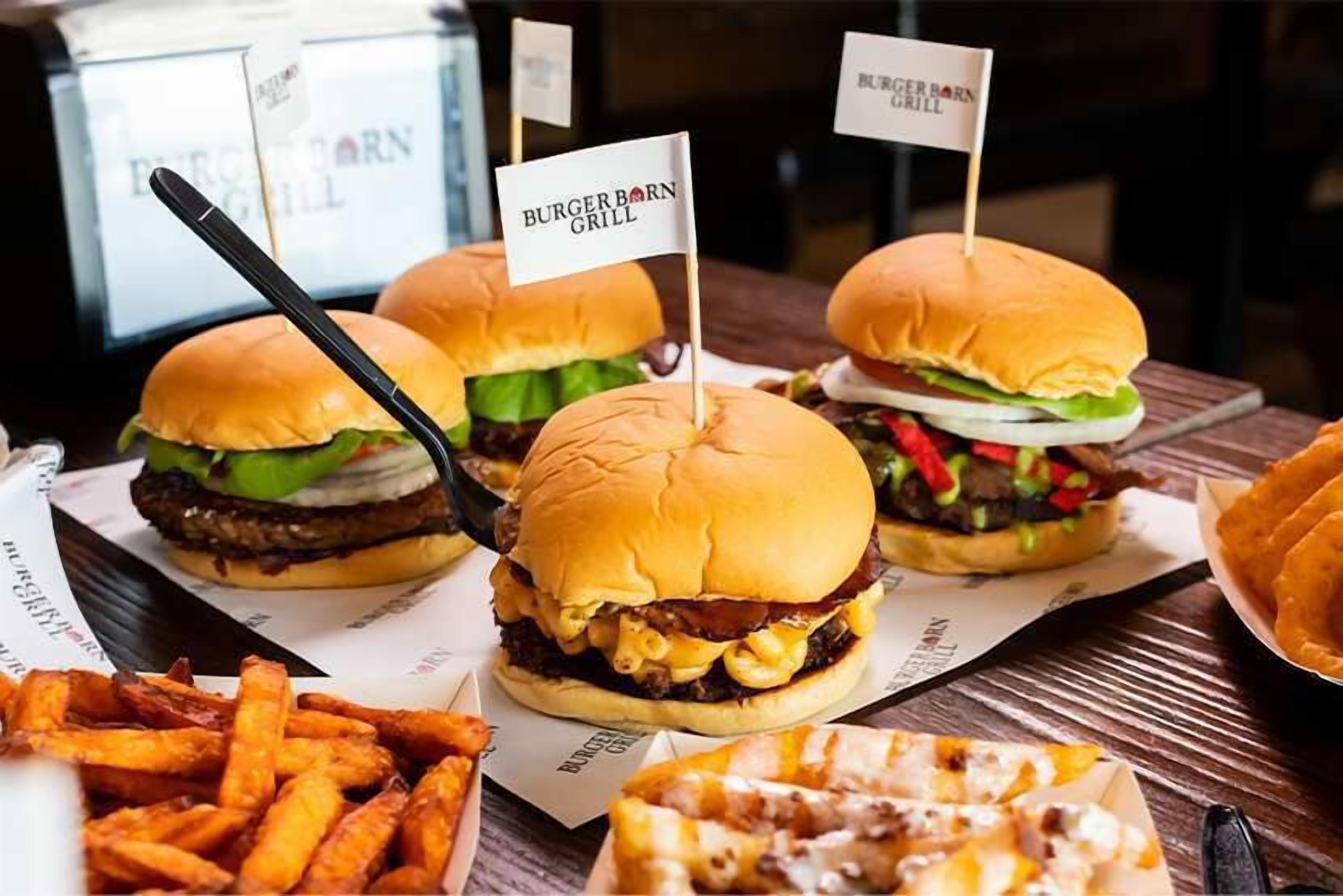 Three burgers with flags, fries, and a pizza on a wooden table.