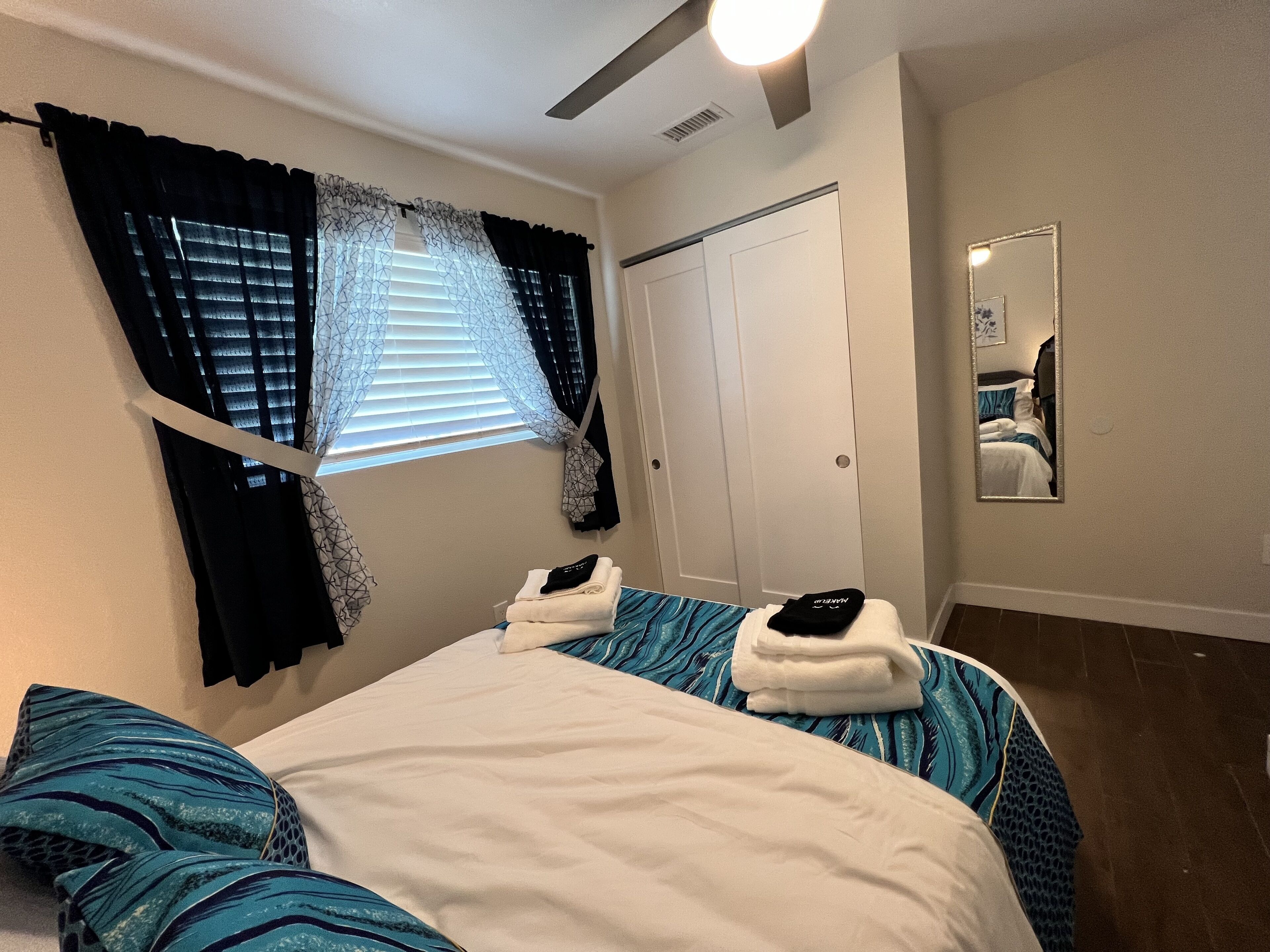 Une chambre à coucher avec un lit, une fenêtre avec des rideaux, un miroir et une porte.