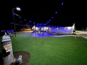 A well-lit outdoor area with artificial grass, a gazebo, and string lights.