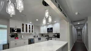 Una cocina moderna con una isla grande de mármol, armarios blancos e iluminación colgante.