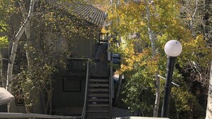 Una escalera de madera que sube hacia un edificio con tejado de tejas, rodeado de árboles con hojas otoñales.