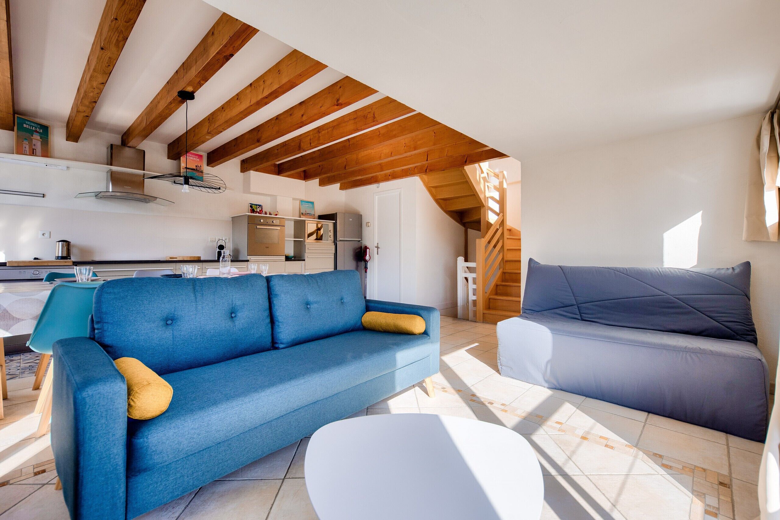 A modern living room with a blue sofa, a white table, and a staircase leading to an upper level.