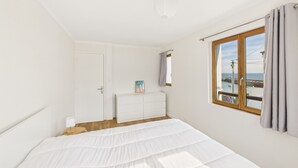 A bedroom with a large bed, a dresser, a window with a view of the sea, and a door. - Sea view - House for 7 with balcony (Saint-Pierre-Quiberon)