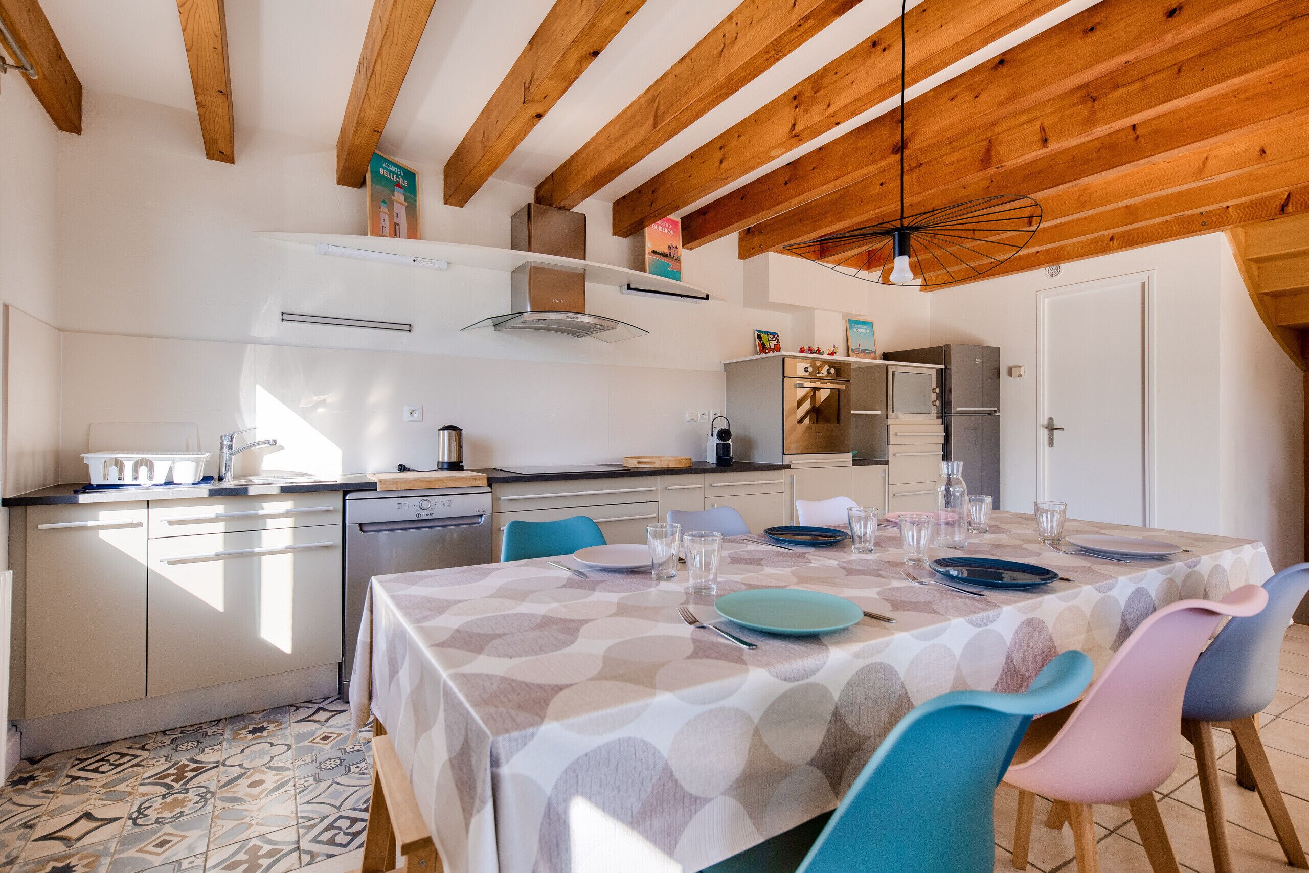 A kitchen with wooden beams, a dining table set for four, and a tiled floor.