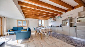 A modern living room with a blue sofa, a dining table, and a kitchen area with white cabinets and a built-in oven. - Sea view - House for 7 with balcony (Saint-Pierre-Quiberon)