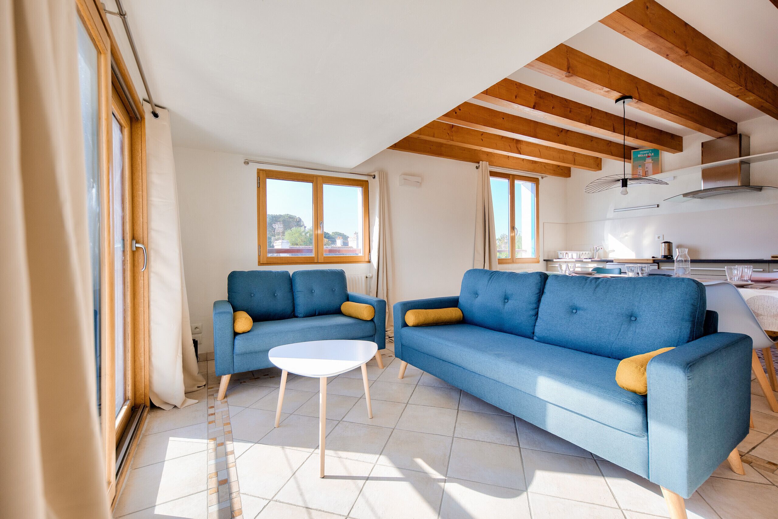 Ein modernes Wohnzimmer mit zwei blauen Sofas, einem weißen Couchtisch und großen Fenstern.