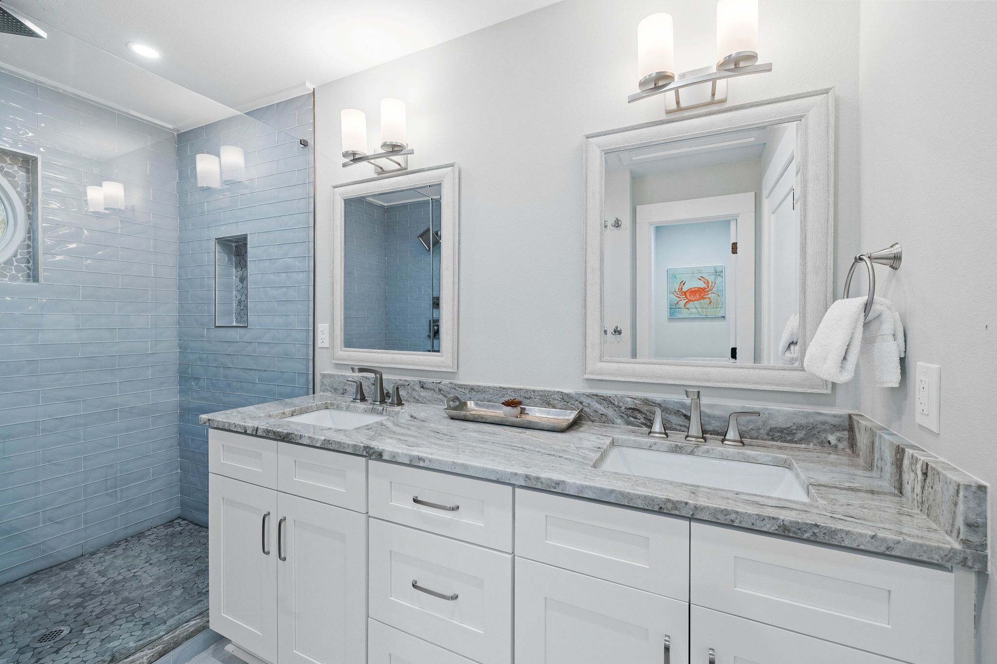 Une salle de bain avec deux lavabos, des meubles blancs et des murs recouverts de carreaux bleus.