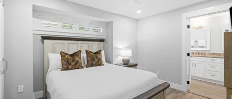 Un dormitorio con una cama grande, una mesita de noche, un ventilador de techo y vistas al baño contiguo.