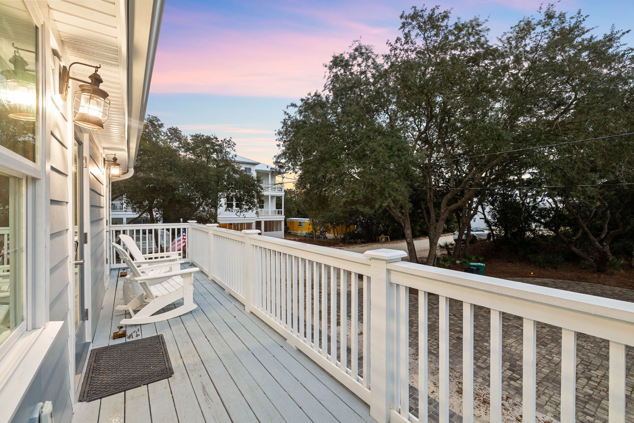 A wooden deck with white railings, a rocking chair, and a porch light.