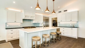 A modern kitchen with white cabinetry, a large island with stools, and copper pendant lighting. - Private Pool, Gas Grill, 2 Smokers, Boat Slip, Huge Deck & Patio & More! (Jamaica Beach)