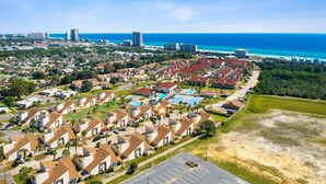 An aerial view of a coastal residential area with multiple-story buildings, a beachfront, and a parking lot.