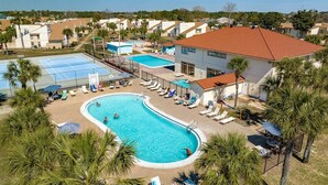 A resort with a large swimming pool, sun loungers, and palm trees.