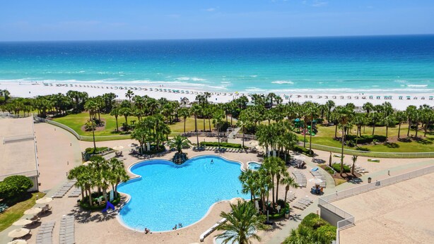 Un resort con una piscina grande, acceso a la playa y palmeras.
