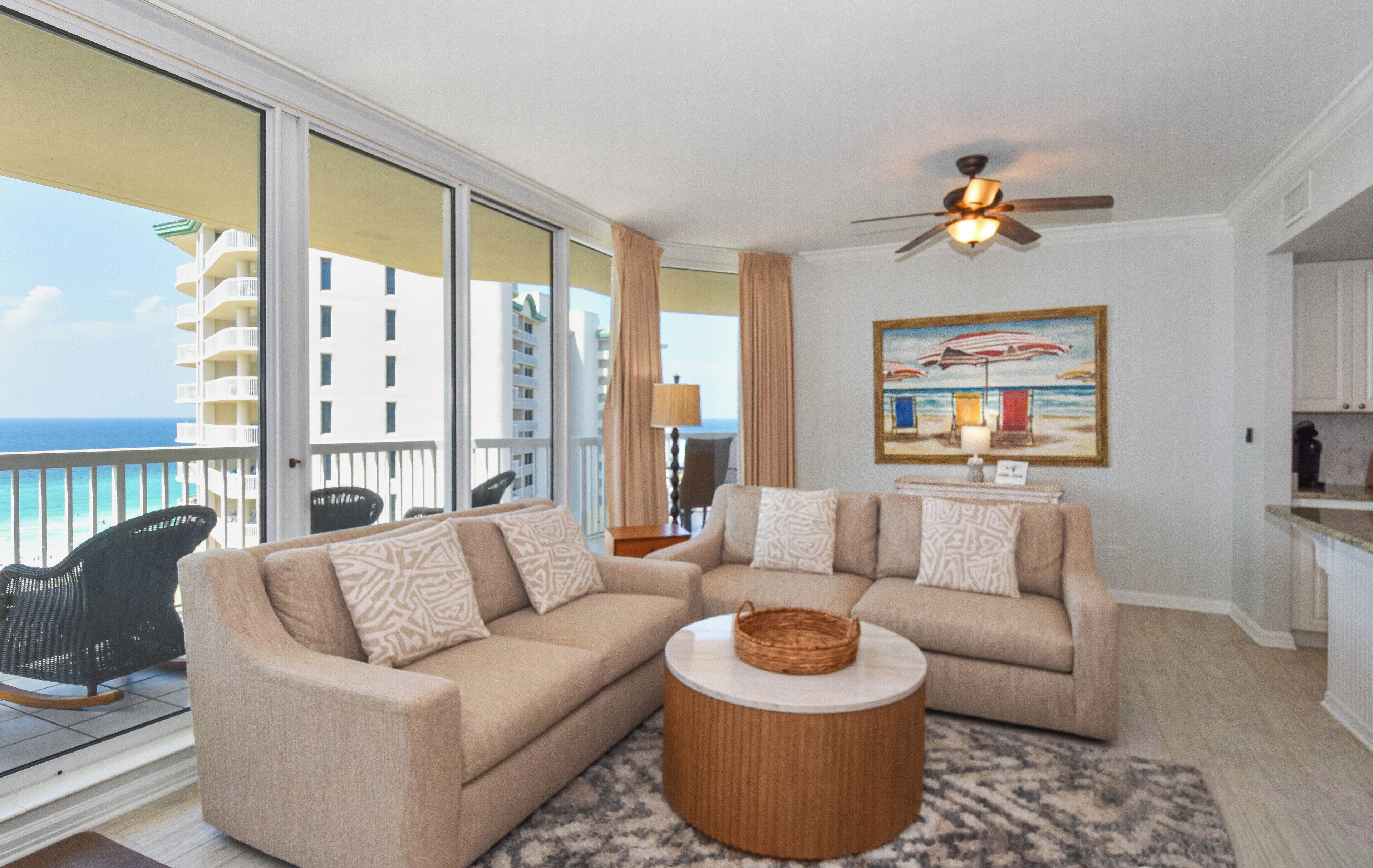 A balcony with a view of a building and the sea. There are two sofas and a round coffee table on the balcony floor.